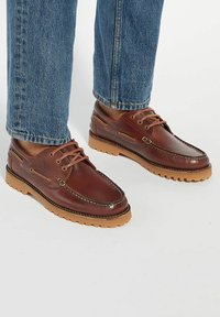 Brown leather shoes with a round toe, cream stitching, and a rubber sole. Features lace-up design with side accents and textured finish.
