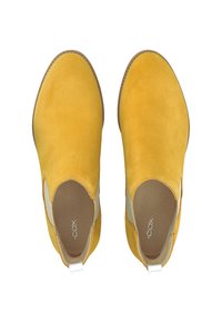 Žluté kotníkové boty z semiše s elastickými bočními panely, kulatou špičkou a hnědou podrážkou. Mají nízký podpatek a poutko na zadní straně.