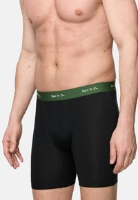 Schwarze Baumwoll-Boxershorts mit grünem Gummibund, der das Markenlogo trägt. Sie haben eine enganliegende Passform und mittellange Beine.