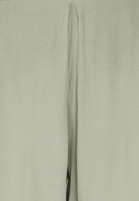 Tissu vert clair avec une surface douce et texturée. Présente une découpe centrale, créant une section ouverte et une forme fluide.