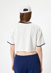 Afskåret hvid T-shirt med marinefarvede detaljer og korte ærmer, parret med marinefarvede joggers. Bagsiden har en simpel halsudskæring og en afslappet pasform.