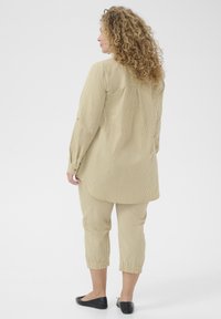 Gestreiftes beige zweiteiliges Outfit mit langärmligem Hemd und verkürzten Hosen. Glatte Textur, lockere Passform, mit elastischen Bündchen und abgerundetem Saum.