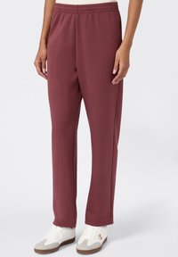 Bordowe dresy z elastycznym pasem, prostym krojem i kieszeniami po bokach. Połączone z białymi trampkami z szarymi akcentami.