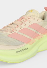 Μπεζ και ροζ αθλητικό παπούτσι με ανοιχτό πράσινο πέλμα, με το κείμενο «Dreamstrike Glow» και τρεις ροζ ρίγες στο πλάι.