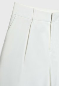 Pantalons plissés blancs en tissu lisse avec une taille cintrée et des poches latérales. Présente un design épuré et minimaliste.