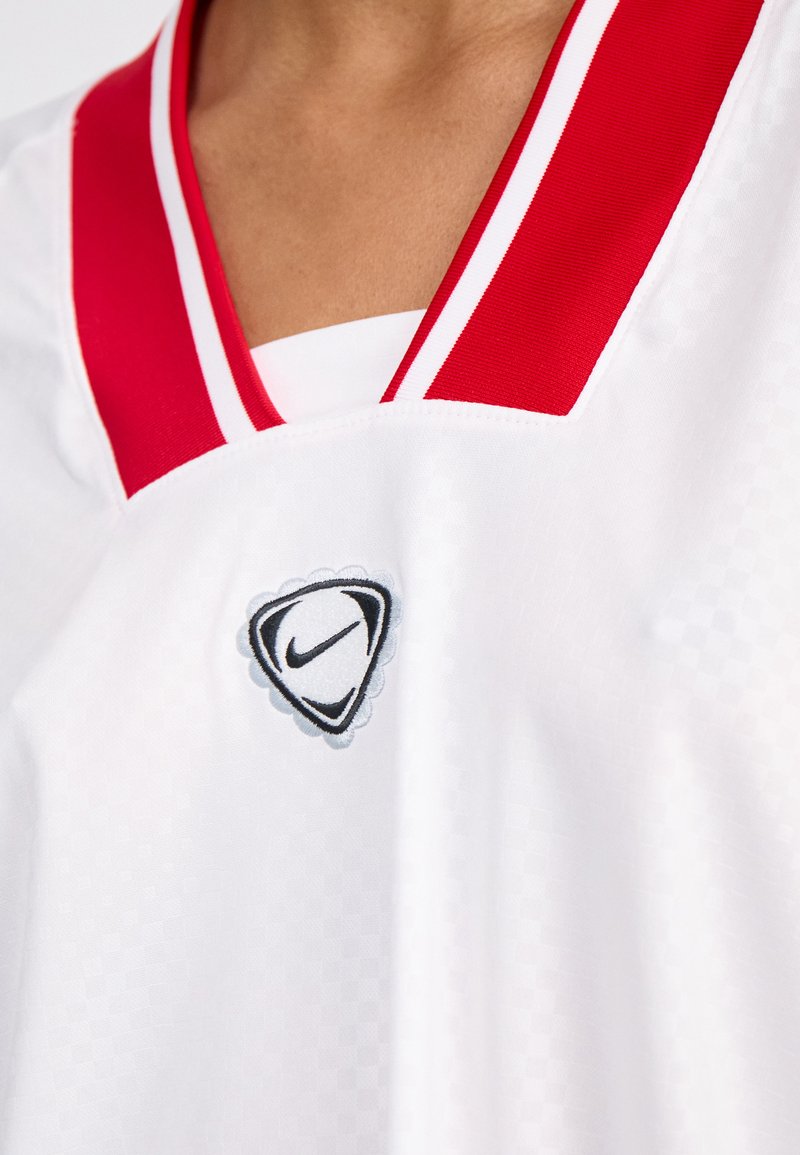 Weißes Sporttrikot mit rotem V-Ausschnitt und weißen Streifen. Enthält ein schwarz-graues Nike-Logo, das auf der Brust gestickt ist.