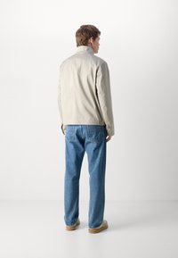 Lys beige jakke med høy krage, lette materialer og en skreddersydd passform. Kombinert med løse blå denimjeans og beige sko.