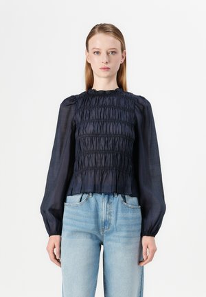 Mørkeblå smocked bluse med lange ærmer, teksturert stoff og rynkede halskant, kombinert med lyseblå høytlivsjeans.