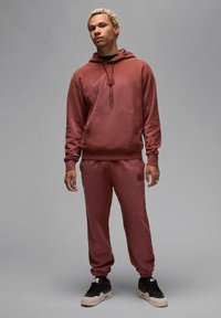 Bordeauxfarbene Kapuzenjacke und passende Jogginghose aus weichem Stoff. Kapuze mit Kordelzügen, Kängurutasche und gerippten Bündchen, kombiniert mit schwarzen Turnschuhen.