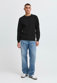 Svart strikket genser med rund hals, kombinert med lys blå rettbente jeans og hvite sneakers med svarte detaljer. Enkelt design, ingen mønstre.