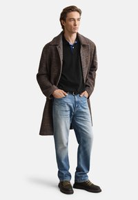 Barna kockás kabát fekete, kék galléros poló fölött, világoskék farmernadrág és arany részletekkel díszített barna túracipő.