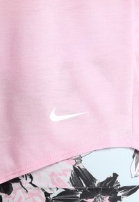 Różowa bawełniana koszulka z krótkim rękawem, z białym logo Nike. Brzeg jest lekko zaokrąglony, o miękkiej teksturze.