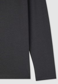 Dettaglio del tessuto e della manica di una camicia a maniche lunghe color grigio scuro su uno sfondo chiaro, che mostra la texture e le cuciture.