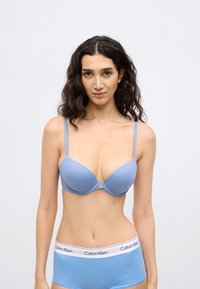 Sutien albastru deschis captușit cu bretele reglabile și design fără cusături, asortat cu pantaloni scurți hipster albaștri cu logo alb pe talie.