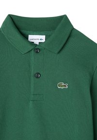 Grön Lacoste polo t-shirt med ribbad krage, två svarta knappar och broderad krokodil-logotyp på vänster bröst.