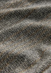Herringbone-patterned fabric in gray shades with brown accents. The texture appears soft and slightly fuzzy, highlighting its wool composition.