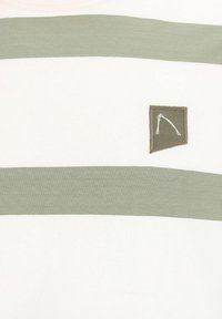 Dryžuota marškinėliai šviesiai grietinėlės ir alyvuogių žalios spalvos. Minkšta medvilnė su apvaliu kaklu, su mažuoju išsiuvinėtu logotipo pleistru kampe.