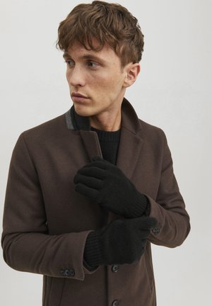 Abrigo marrón con un corte entallado, acento en el cuello gris y guantes de punto negros. Los guantes tienen una textura acanalada y un diseño ajustado.