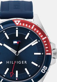 Navy-blå gummirem ur med rustfrit stål hus. Rund urskive med en mørkeblå talp, hvide timemarkører, rød og hvid bezel samt logo.