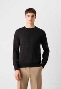 Pull-over en tricot noir avec un col rond et des manches longues. Présente un ourlet et des poignets côtelés, fabriqué en tissu doux avec une texture lisse.