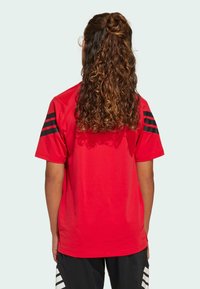 Rotes Kurzarm-T-Shirt mit schwarzen Streifen auf jeder Schulter. Hergestellt aus einem leichten Stoff mit einer glatten Textur. Rückansicht gezeigt.