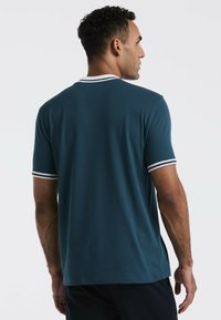 Teal poloshirt met korte mouwen en witte strepenaccenten op de kraag en mouwen; gemaakt van soepele stof met een ontspannen pasvorm, met een eenvoudig ontwerp aan de achterkant.