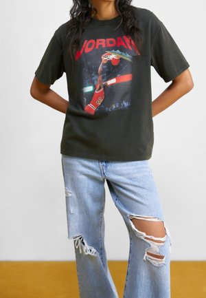 Czarny bawełniany T-shirt z grafiką przedstawiającą koszykarza wykonującego wsad; zestawiony z jasnoniebieskimi, postarzanymi jeansami z rozdarciami na kolanach.