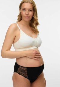 Trudnička majica nježne krem boje, s nabranoj tkaninom; uparena s crnim gaćicama koje imaju čipkast bočni panel i glatki finiš.