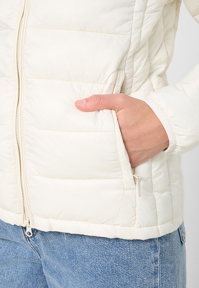 Giacca a vento bianca con texture trapuntata, zip frontale e tasche laterali. Materiale morbido con un design aderente, ideale per essere indossata a strati.