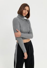Pull à col roulé gris côtelé avec des manches longues, longueur cropped. Associé à un pantalon de survêtement noir avec des rayures blanches sur les côtés et une taille à cordon.