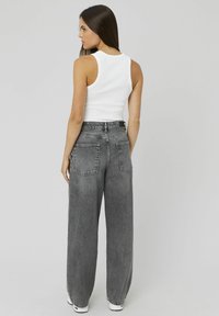 Un débardeur blanc à côtes associé à un jean en denim gris à taille haute et à pattes d'éléphant, doté de deux poches arrière et d'une coupe décontractée.