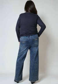 Marineblauwe longsleeve top van lichtgewicht stof, gecombineerd met wijde blauwe denim spijkerbroeken met twee achterzakken met decoratieve ritsen.