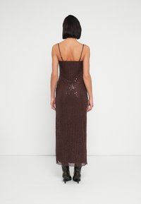 Καφές φόρεμα με παγιέτες με εφαρμοστή σιλουέτα, λεπτές spaghetti τιράντες και μακρύ μήκος, συνδυασμένο με μαύρες μπότες με τακούνι.