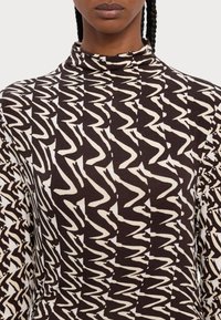 Haut à manches longues avec un col montant, présentant un motif abstrait en zigzag marron et crème sur un tissu doux.