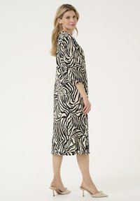 Zebra print dress featuring a loose fit, long sleeves, and knee-length design in cream and black fabric. Smooth texture with no visible hardware.
