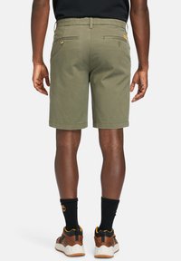 Khaki shorts med en skræddersyet pasform, der har to baglommer og subtile syninger. Bæres med brune sko og sorte sokker.