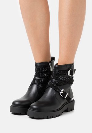 Pitonere in pelle nera con cinturini testurizzati, hardware in argento e suola spessa. Le bottine presentano una chiusura con zip e sono decorate con accenti scintillanti.