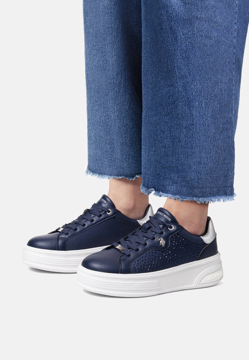 Marina lädersneakers med perforerade detaljer, vit plattformssula, snörning och silveraccenter, i kombination med fransat denim.