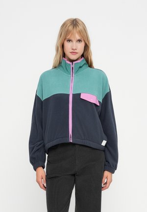 Veste courte en polaire teal, marine et rose. Dotée d'un col montant, d'une fermeture éclair sur le devant et d'une poche à pression. Texture douce avec des poignets côtelés.