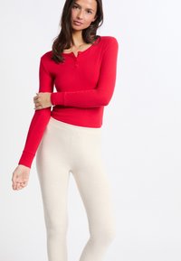 Top de henley de manga larga roja con detalles de botones, combinado con leggings de color crema. Ambos artículos tienen una textura suave y ajustada.