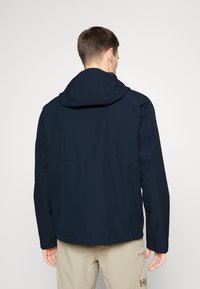 Chaqueta impermeable azul marino con capucha, que presenta una textura suave, un diseño simple y puños ajustables. La vista trasera no muestra ninguna marca visible.