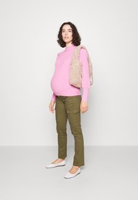 Pink ribbed sweater, olive green cargo pants, and white ballet flats. Holding a beige fuzzy bag with one strap.