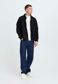 Black fleece jacket with button closures, front pockets, layered over a white shirt. Worn with dark blue denim pants and white sneakers.