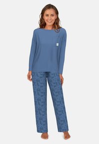 Blauwe long-sleeve top met een zak, gecombineerd met blauwe pyjamabroek met een patroon van geometrische ontwerpen. Zachte stof, ontspannen pasvorm.