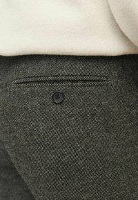 Sive herringbone hlače s teksturiranim završetkom, koje imaju mali crni gumb na stražnjem džepu i uredno prošivene detalje.