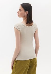Beige, ribbet kortærmet top med rund halsudskæring, stylet med olivengrønne bukser. Stoffet fremstår glat med en subtil struktur.