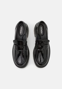 Mocassins en cuir verni noir avec l'avant relevé et une semelle intérieure rembourrée, présentant une texture lisse et brillante et une semelle noire épaisse.