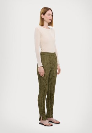 Light beige long-sleeve top with a round neckline, paired with olive green crinkled pants. Model wears black sandals with silver accents.