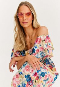 Kwiatowa sukienka na ramiączkach w kolorach różowym, niebieskim i żółtym, zestawiona z gradientowymi różowymi okularami przeciwsłonecznymi oraz kolorową naszyjnik z koralików.