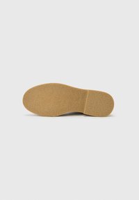 Suela de zapato con un material de goma marrón claro texturizado. Presenta una forma redondeada y un patrón sutil para mayor tracción.